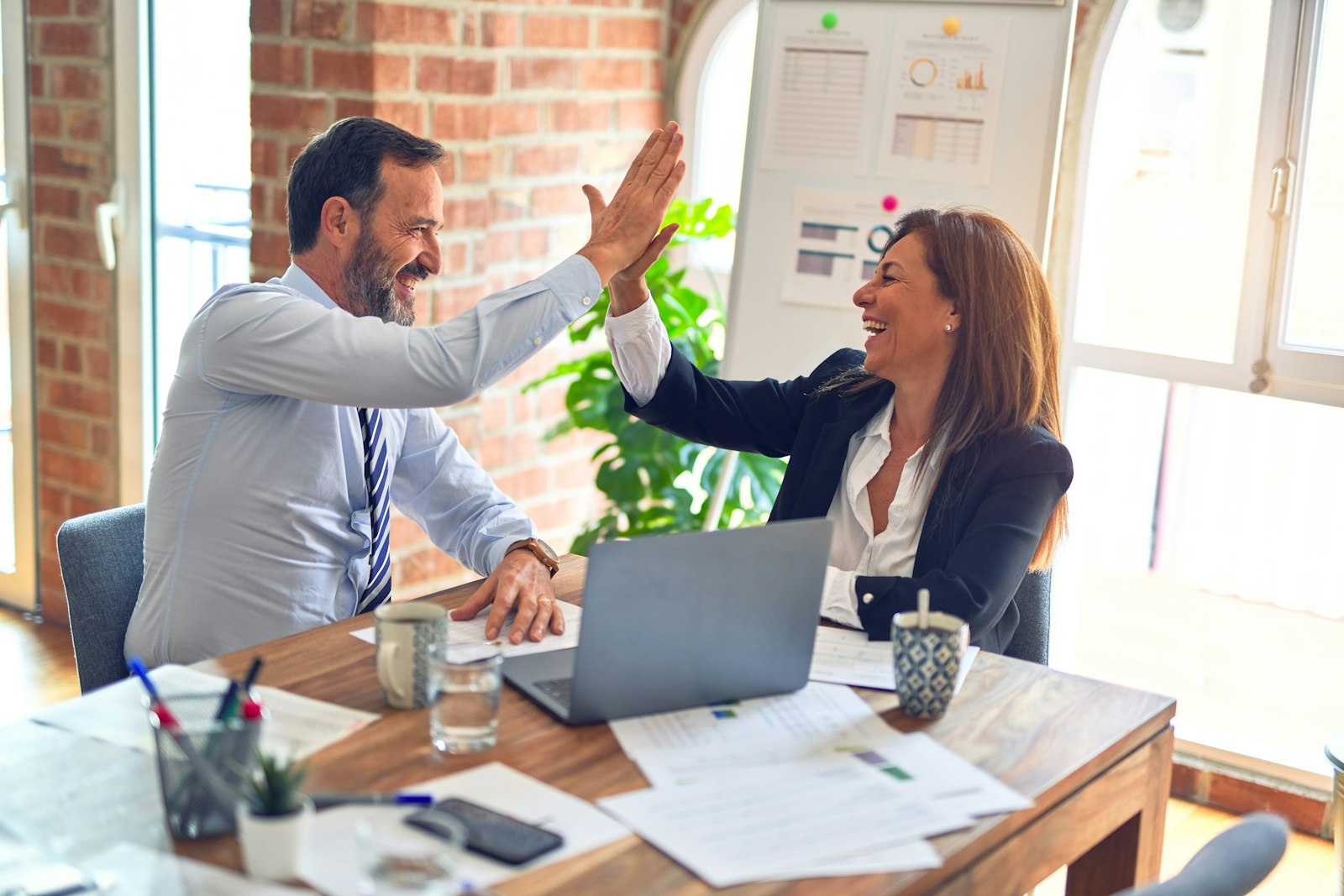 Two colleagues at a desk giving each other a high five