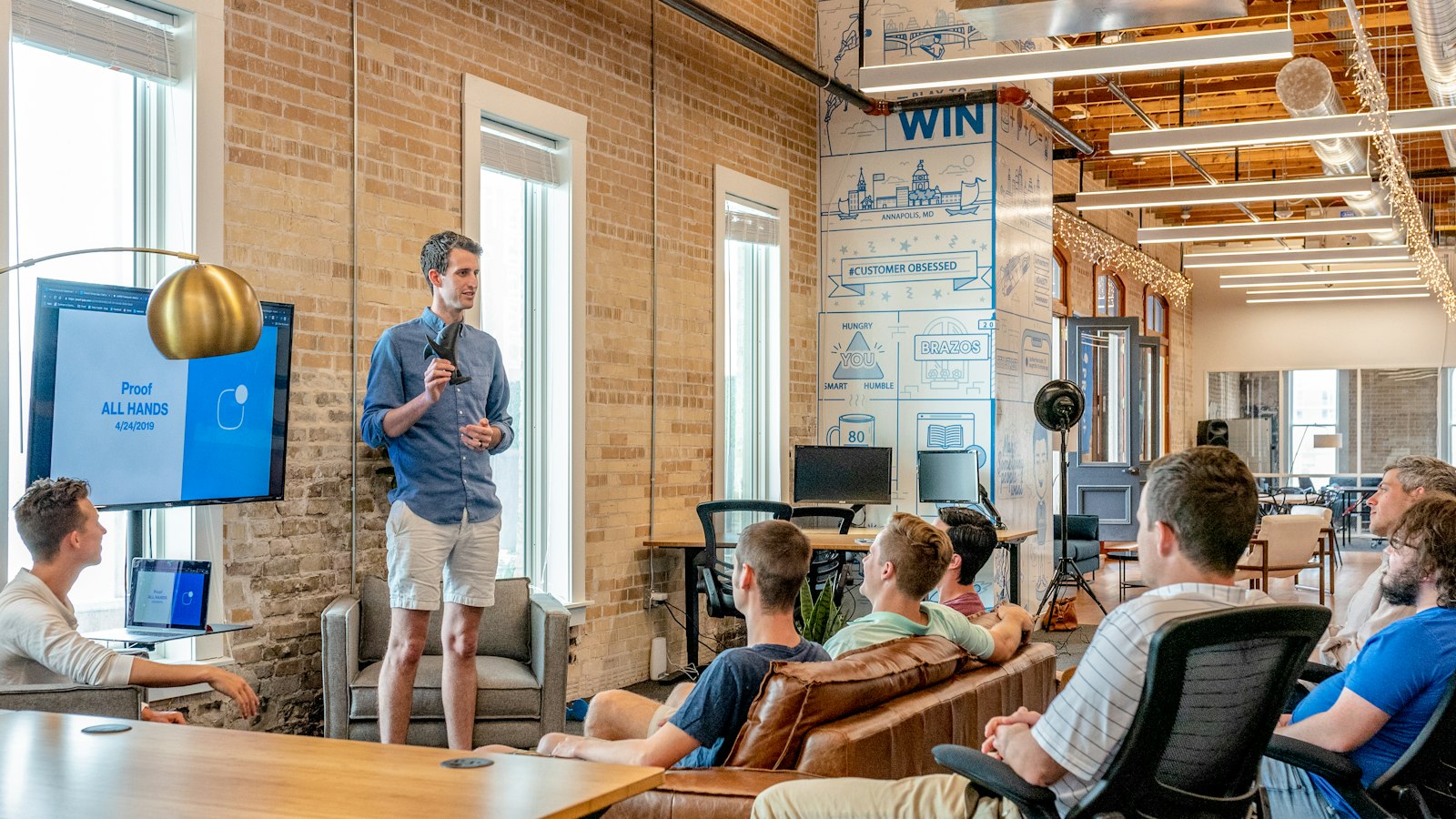 A presenter talking to a team seated on sofas in a bright office